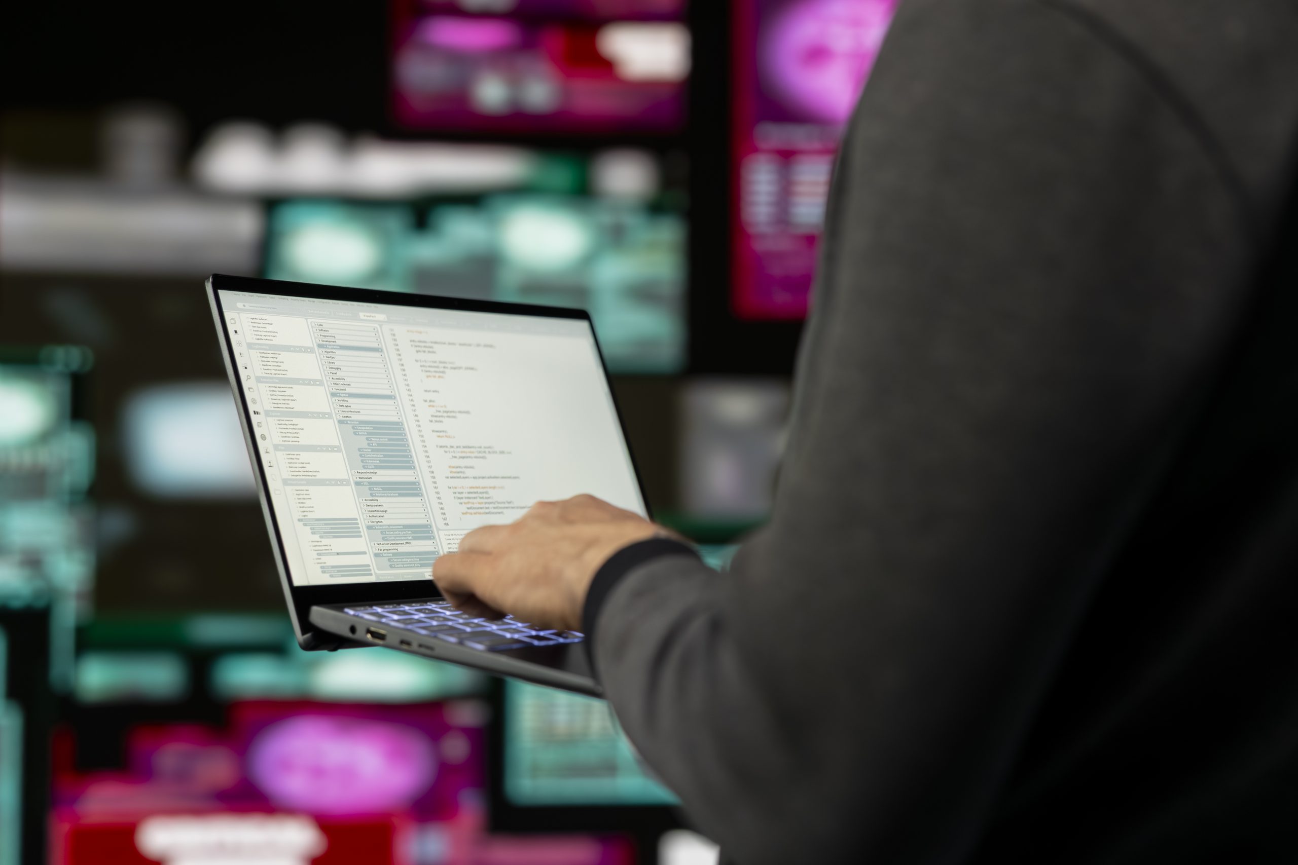 Persona strādā ar portatīvo datoru, ekrānā redzams programmēšanas kods, simbolizējot kiberdrošību un investīciju krāpšanu tiešsaistē.