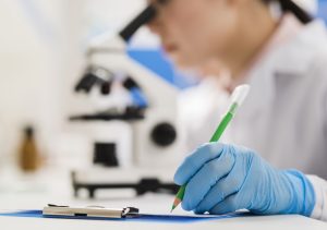 Laboratorijas darbiniece ar cimdiem pieraksta medicīniskos datus skrīninga izmeklējumam