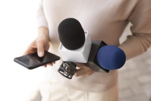 Žurnālists tur mikrofonus un viedtālruni, gatavojoties intervijai.
