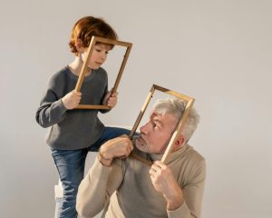Vīrietis un zēns tur rokās tukšus foto rāmjus un skatās viens uz otru