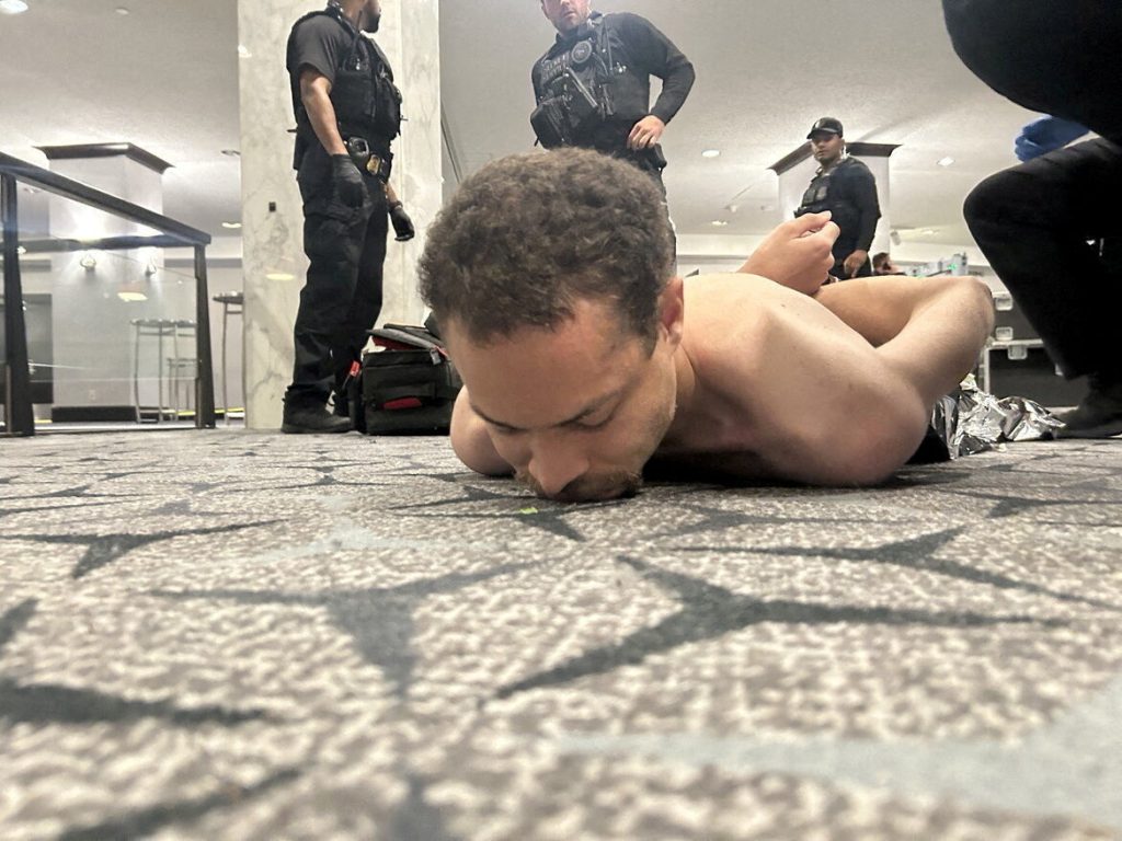 Vīrietis noguldīts uz zemes, apkārt policijas darbinieki