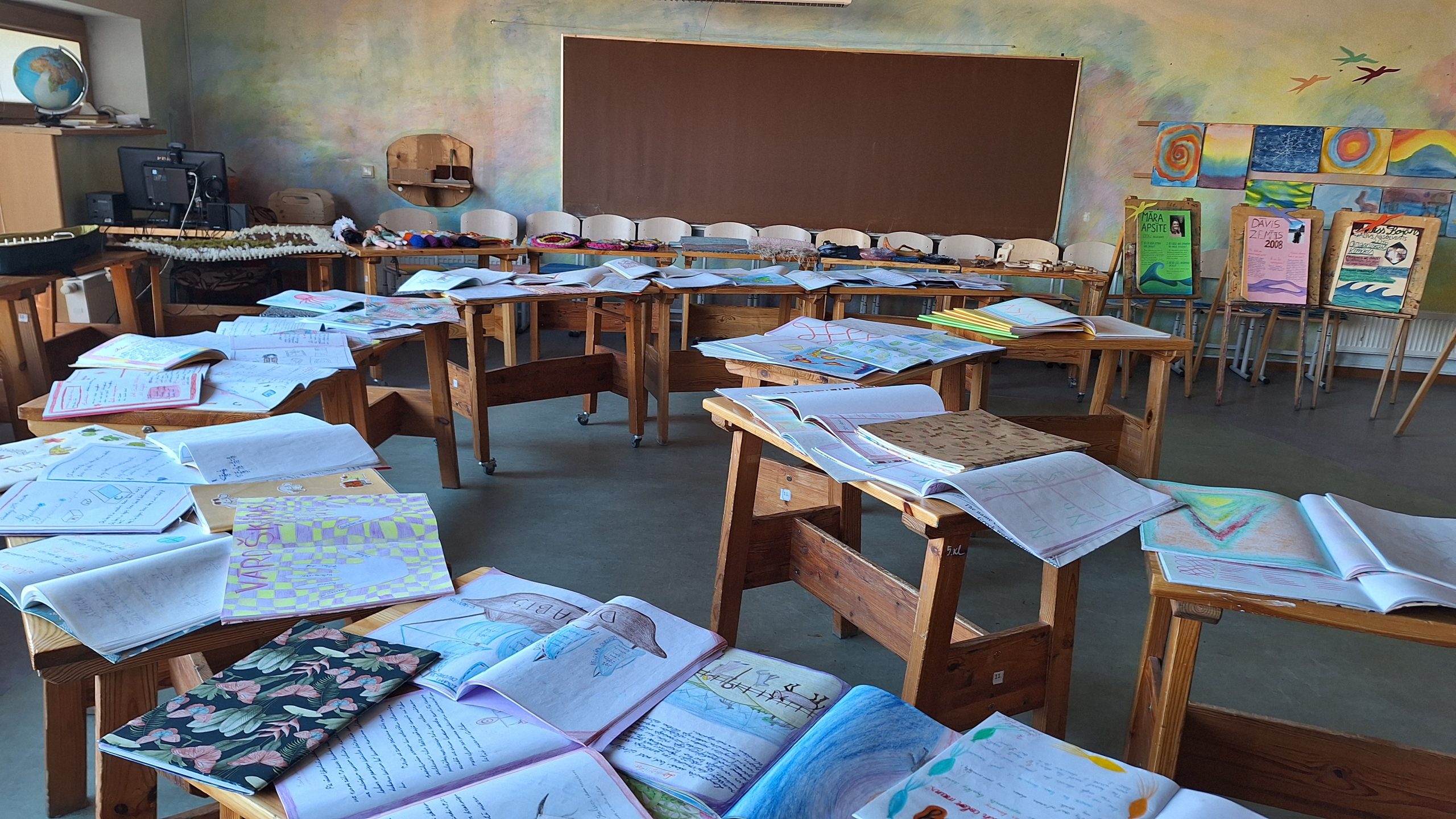 Valdorfa skolas klase ar skolēnu darbiem un mācību materiāliem uz galdiem.