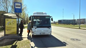 Autobuss pieturā uzņem pasažierus saulainā dienā