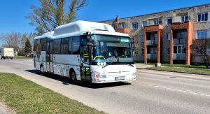 Balts pilsētas autobuss brauc pa ielu dzīvojamā rajonā
