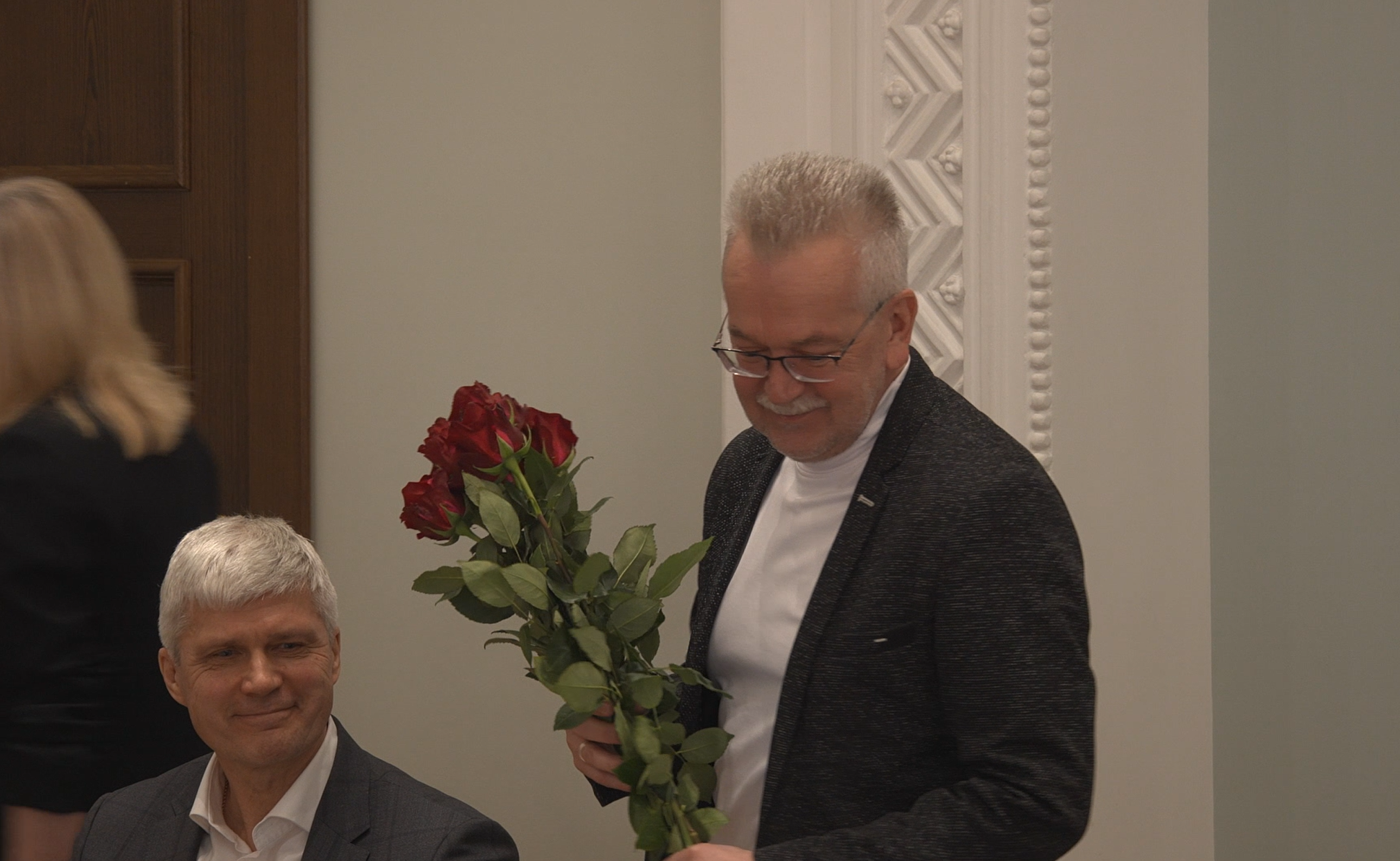 Vīrietis pasniedz sarkanas rozes pasākuma laikā telpā