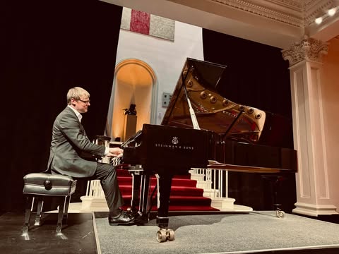 Pianists uz skatuves spēlē flīģeli koncertzālē