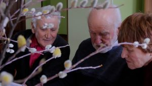 Seniori kopā aplūko materiālus pie galda, priekšplānā pūpoli