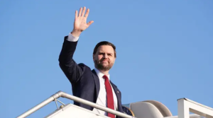 ASV viceprezidents Džeimss Deivids Venss sveicina, stāvot uz lidmašīnas trapa.