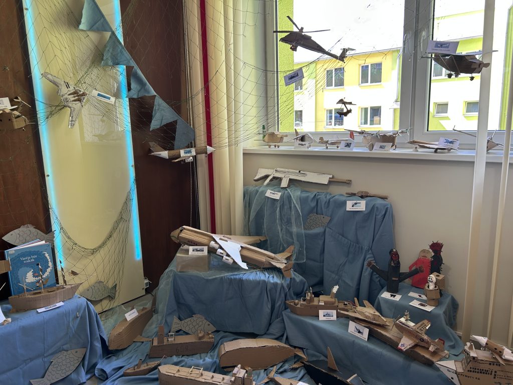 Kartona modeļi izkārtoti pie loga uz galdiem