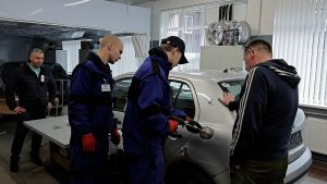 Cilvēki darbnīcā veic auto virsbūves remontu pie aizmugurējā sāna paneļa