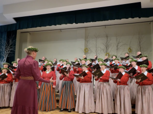 Koris tautastērpos dzied uz skatuves diriģentes vadībā