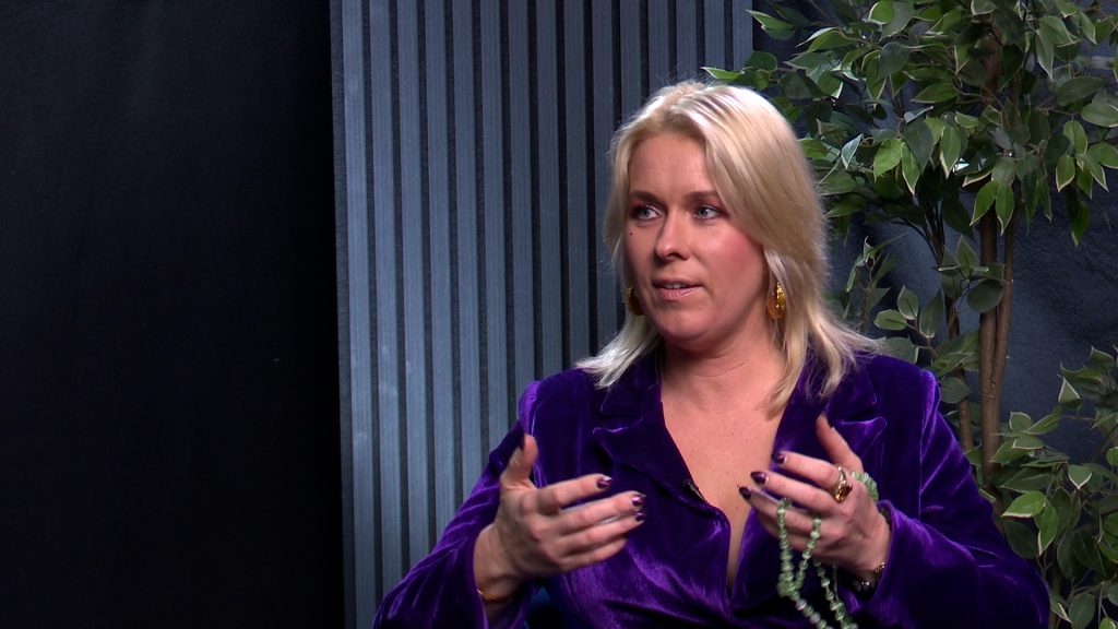 Liene Šomase studijā intervijas laikā, runā un žestikulē ar rokām