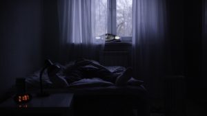 Vīrietis naktī guļ nomodā gultā tumšā istabā, redzams bezmiegs un vientulība
