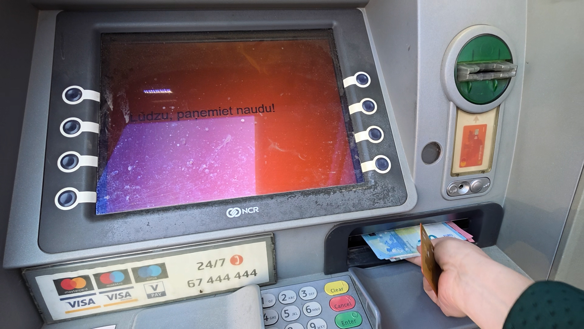Cilvēks izņem skaidru naudu no bankomāta.
