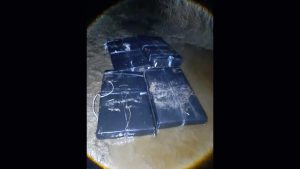 Robežsargu naktī nofotografēts plosts ar melnā plēvē iepakotām kontrabandas cigaretēm seklā ūdenī pie Daugavas krasta.