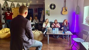 Neliela iekštelpu diskusija radošā telpā ar cilvēkiem, kas klausās runātāju.