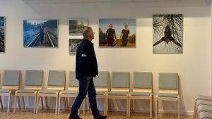 Fotogrāfiju izstāde uz sienas Jēkabpils Tautas namā ar apmeklētāju
