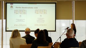 Cilvēki klausās prezentāciju par darbu daudzvalodu vidē konferenču telpā