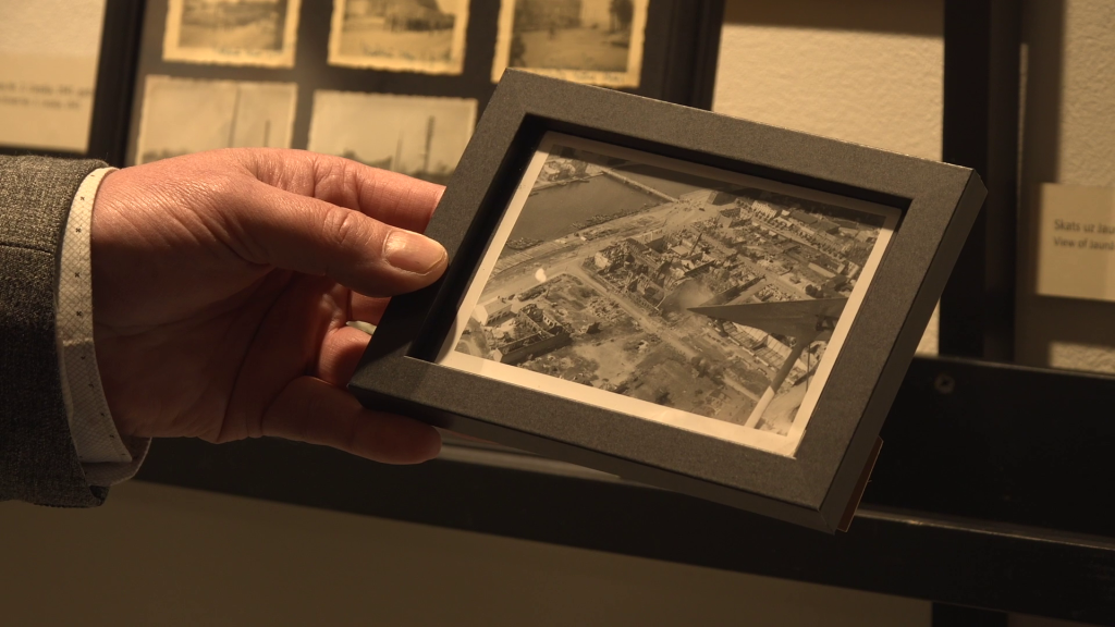 Rokā turēta ierāmēta vēsturiska fotogrāfija ar Liepājas skatu no augšas