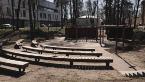 Āra amfiteātris ar koka sēdvietām un apaļu skatuvi parka vidē.