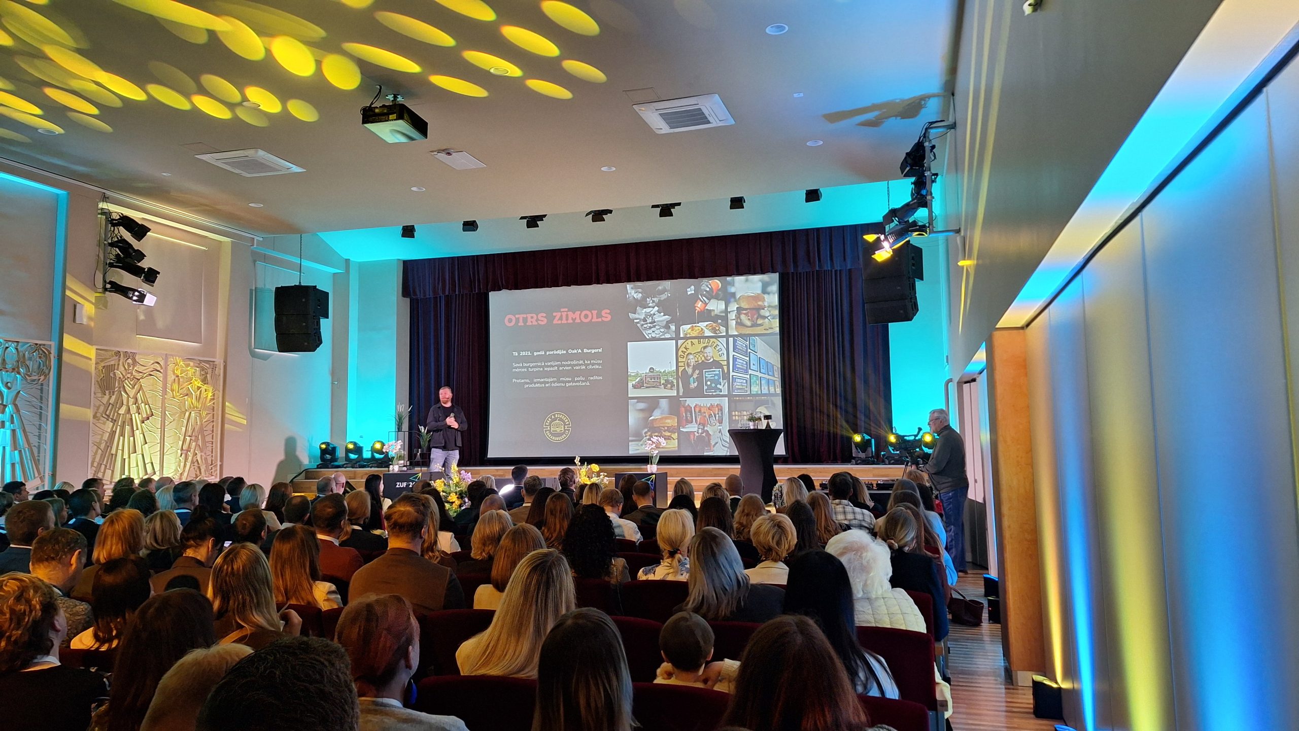 Uzņēmēju forums konferenču zālē ar prezentāciju uz skatuves