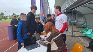 Skolēni stadionā reģistrējas sporta aktivitātēm pie organizatoru galda