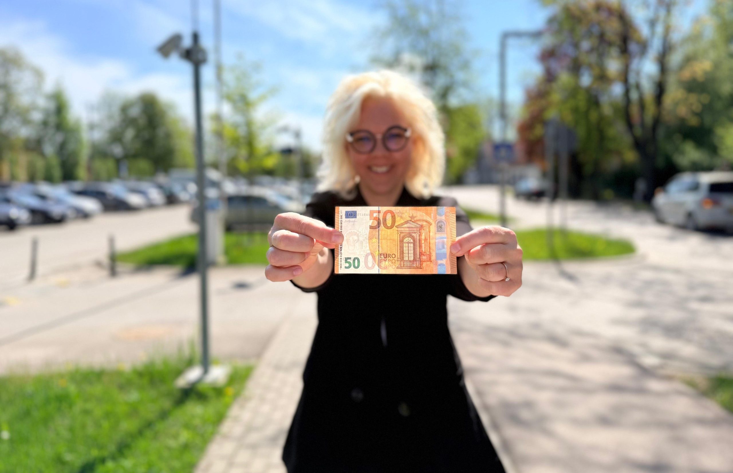 Sieviete ārā tur rokās 50 eiro banknoti.