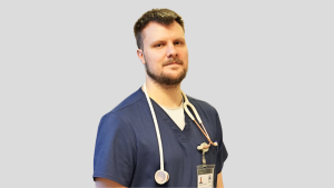 Ārsts Aleksandrs Talanovs zilā mediķa formā ar stetoskopu ap kaklu