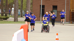 “Wings for Life World Run” dalībnieki skrien kopā ar cilvēku ratiņkrēslā