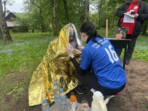 Jauniete sniedz palīdzību cilvēkam, kurš ietīts termo segā pirmās palīdzības mācībās parkā