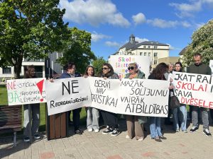 Pie Bauskas novada domes cilvēki piketē pret plānoto skolu reorganizāciju, rokās turot plakātus.