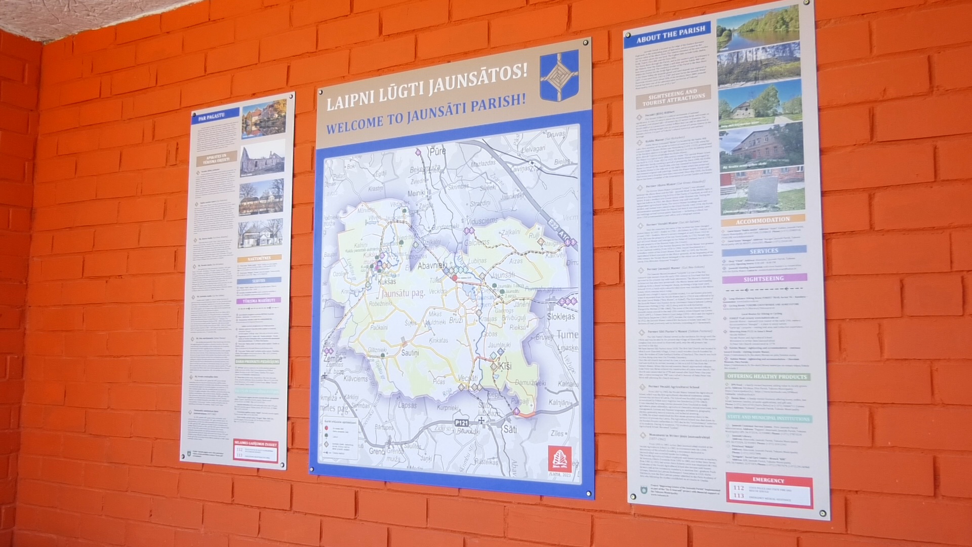 Informācijas stends ar Jaunsātu pagasta karti un aprakstu uz oranžas sienas.