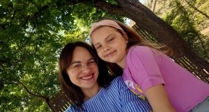 Mamma ar meitu ārā zem koka, smaidot kopīgā ikdienas brīdī