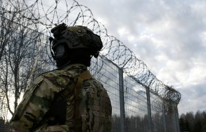 Militārpersona pie žoga ar dzeloņstiepļu norobežojumu uz Latvijas robežas