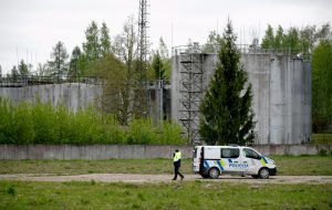 Policijas automašīna pie industriālas teritorijas ar lielām rezervuāru tvertnēm