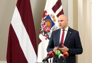 Politiķis preses konferencē pie mikrofoniem un Latvijas karogiem, runājot par politiskajiem procesiem un valdības veidošanu.