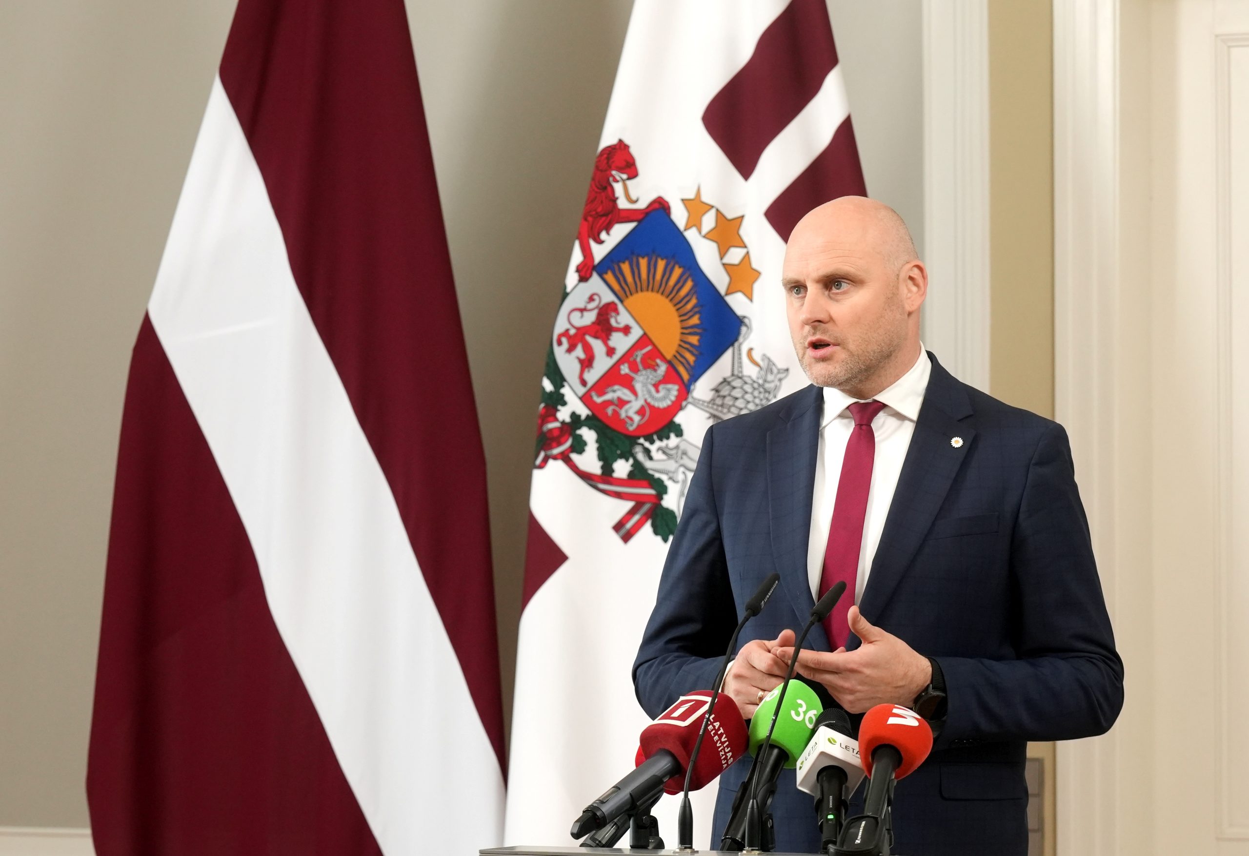 Politiķis preses konferencē pie mikrofoniem un Latvijas karogiem, runājot par politiskajiem procesiem un valdības veidošanu.