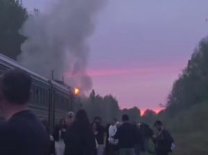 Pasažieri evakuējas no dīzeļvilciena, no kura paceļas dūmi un redzamas liesmas