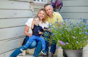 Laura Lakačauska ar ģimeni pie mājas lieveņa vasaras ziedu ieskāvumā