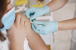 Medicīnas darbinieks ar cimdiem veic vakcināciju pacientam plecā medicīnas iestādē.