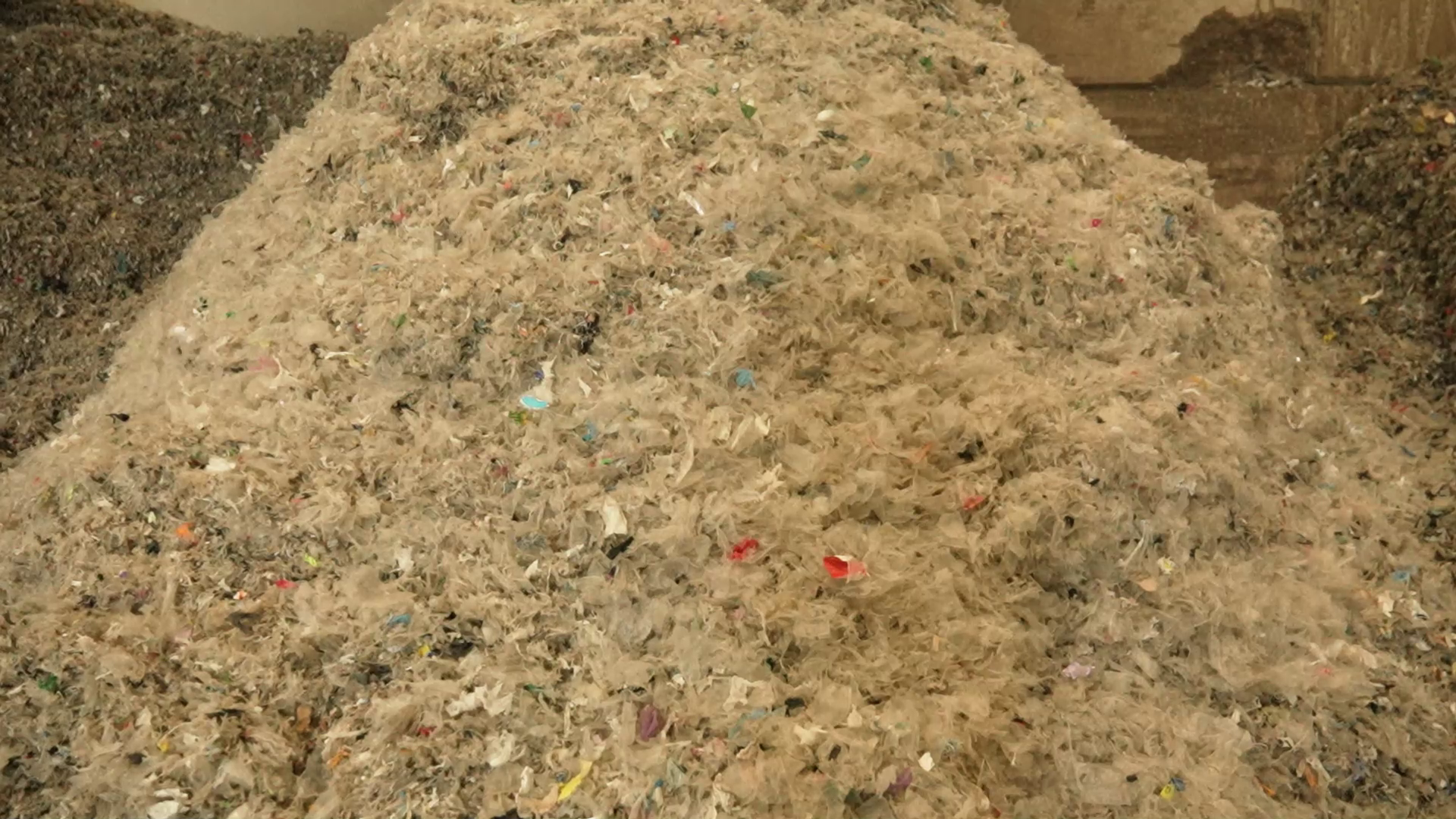 Sasmalcinātu plastmasas un iepakojuma atkritumu kaudze pārstrādes uzņēmumā.