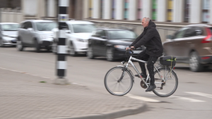 Vīrietis ar velosipēdu šķērso ielu pilsētā
