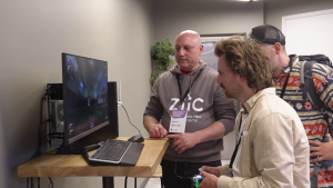 Dalībnieki izmēģina digitālu spēli vai simulāciju pie datora demonstrācijas stendā