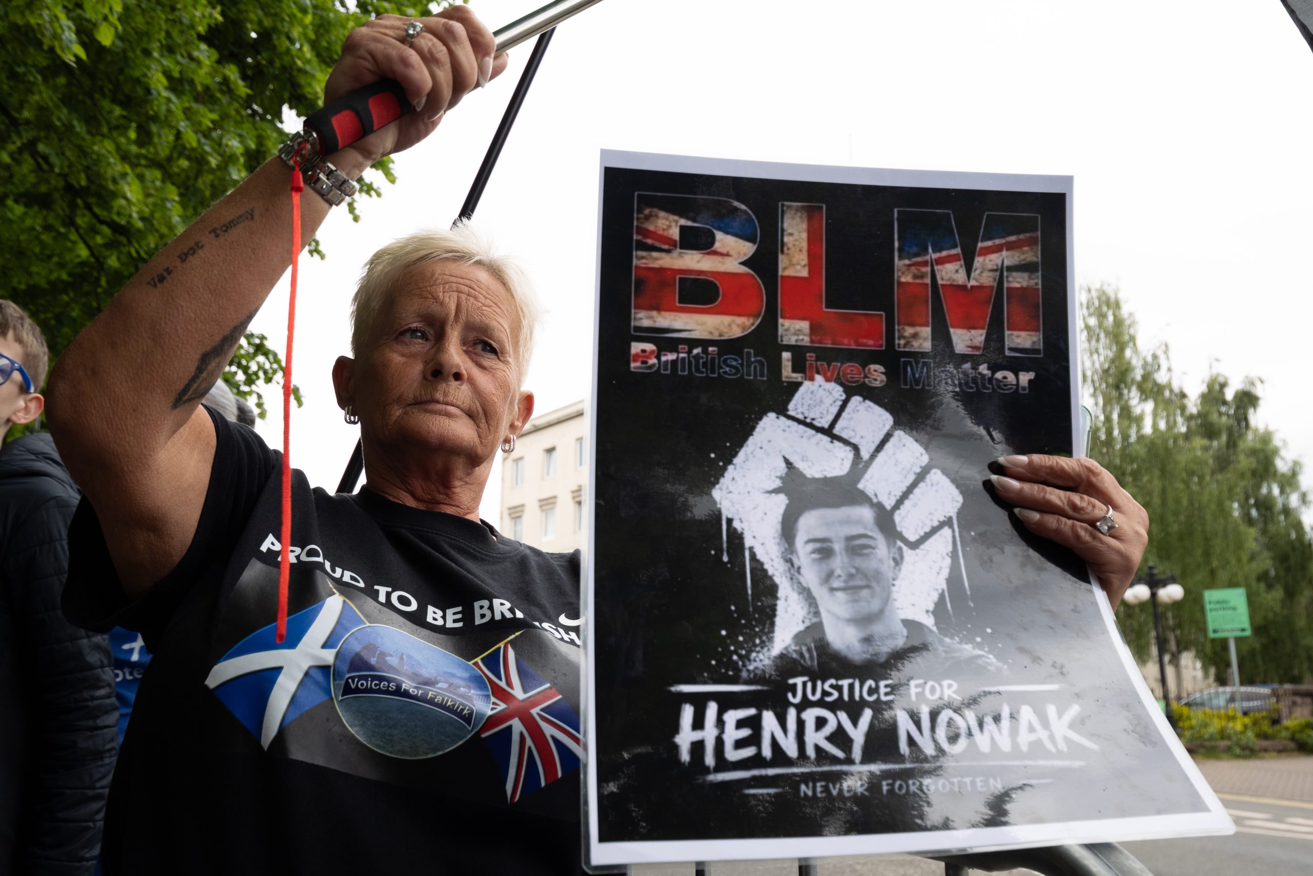Sieviete protesta laikā Skotijā tur plakātu ar uzrakstu “Justice for Henry Nowak” un “British Lives Matter”.
