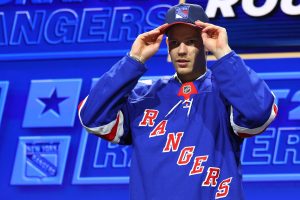 Latvijas hokejists Alberts Šmits pēc izvēles NHL draftā pielaiko Ņujorkas "Rangers" cepuri un kreklu.