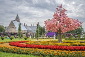 Wagenkull pils parks Dienvidigaunijā ar krāšņām ziedu dobēm, rozā ziedošu koku un vēsturisko pili fonā.