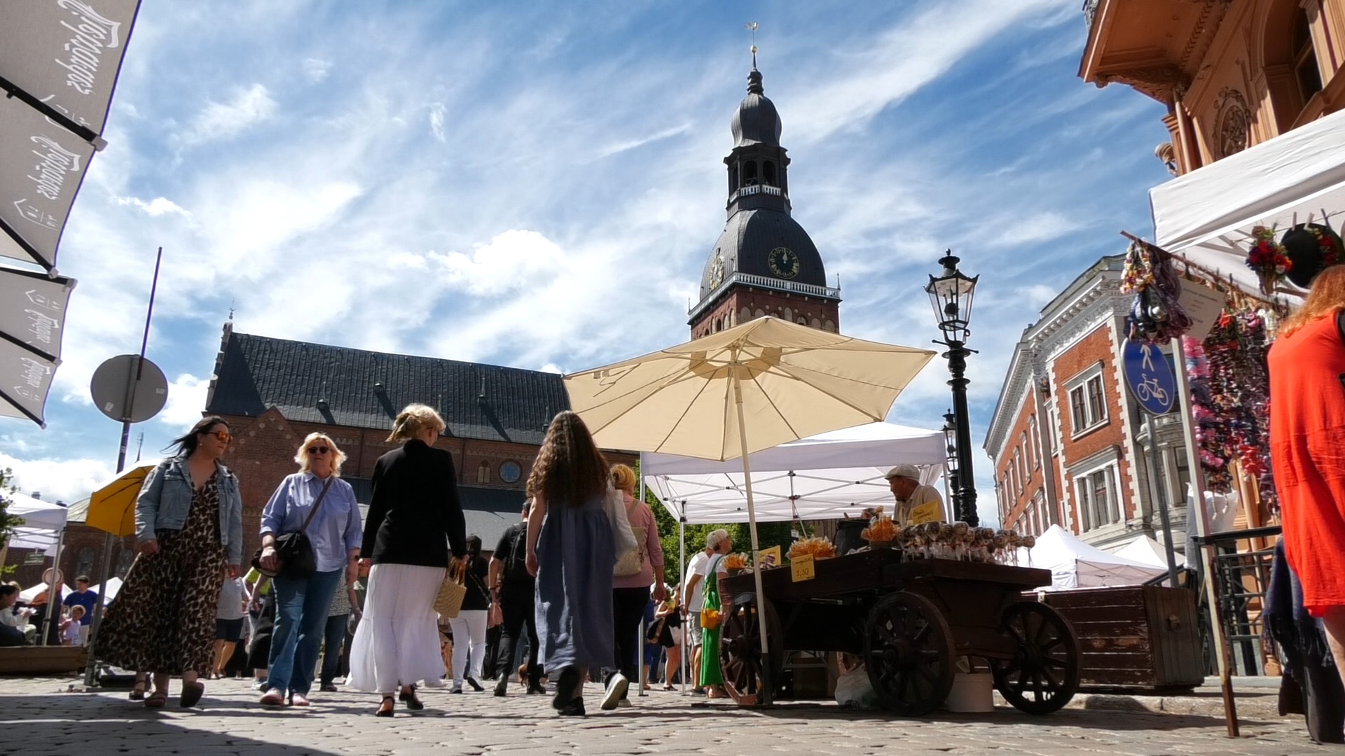 Zāļu tirgus Doma laukumā Rīgā ar tirgotājiem, apmeklētājiem un Rīgas Doma torni fonā.