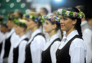 Sievietes tautastērpos ar ziedu vainagiem piedalās svinīgā pasākumā.