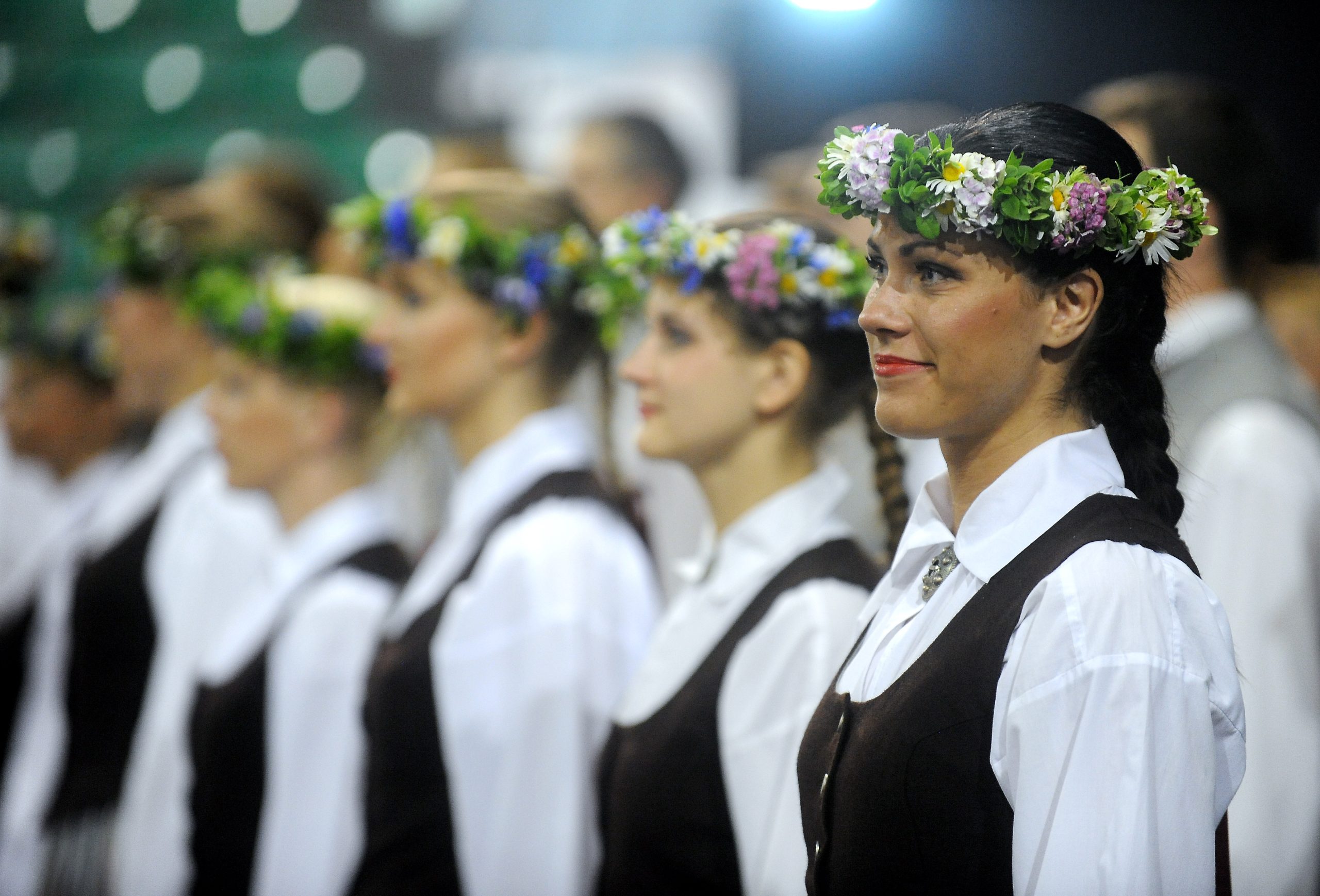 Sievietes tautastērpos ar ziedu vainagiem piedalās svinīgā pasākumā.