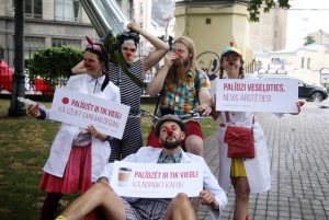 Dr.Klauns kustības pārstāvji ar sarkanajiem klaunu deguniem Vērmanes dārzā tur plakātus vasaras kampaņas atklāšanas pasākumā.